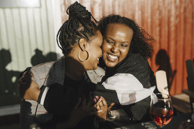 Cheerful young woman embracing female friend during dinner party