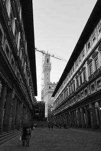 People walking on street amidst buildings in city against sky