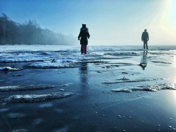 Rear view of silhouette man walking on beach during winter