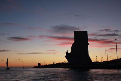 Silhouette city by sea against sky during sunset