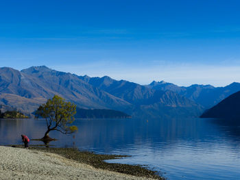 Man sitting on mountain by lake against blue sky