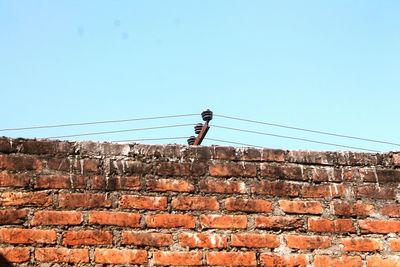 Low angle view of brick wall against cables and clear sky