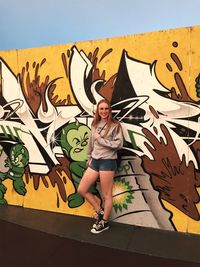 Full length portrait of young woman standing against graffiti wall