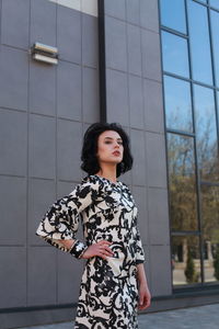 Fashionable young woman wearing floral patterned dress standing against building in city