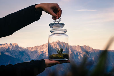 Midsection of person holding glass jar against mountain