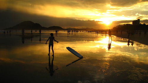 Silhouette people at beach against sky during sunset