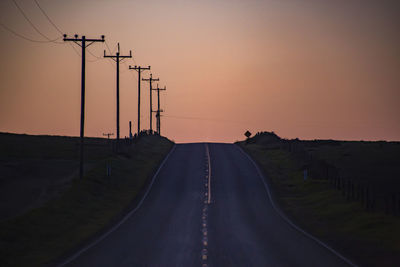 Road amidst silhouette landscape against clear sky during sunset