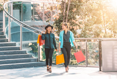 Happy friends with shopping bags walking on elevated walkway