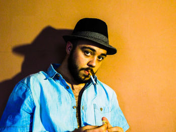 Portrait of young man smoking cigarette against wall