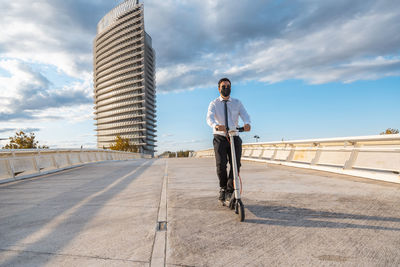Man riding bicycle on city street against sky