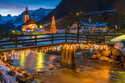 Illuminated buildings by river against sky at night during winter