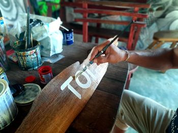 Midsection of man writing text on wooden plank with paint