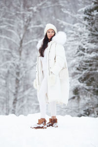 Young fashionable woman wearing stylish white winter puffer coat, knitted hat, mittens outdoors