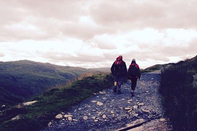 Rear view of people walking on mountain road against cloudy sky