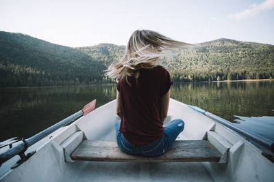 Rear view of woman sitting on boat against lake