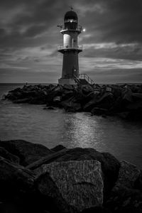 Lighthouse by sea against cloudy sky at night 