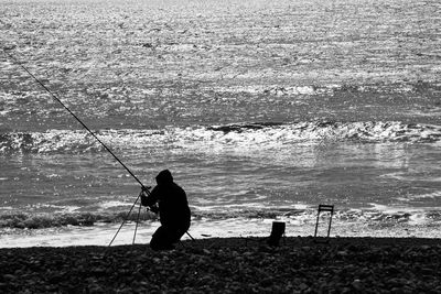 Rear view of silhouette man standing at beach against sky