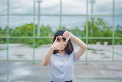 Portrait of young woman gesturing while standing on wet road in park during rainy season