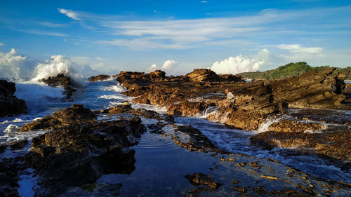 Man fishing while standing on rock by sea