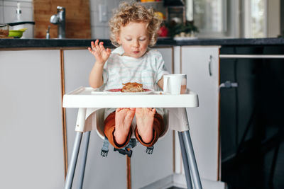 Kid boy sitting in high chair eating homemade apple pie and drinking juice. toddler enjoying food