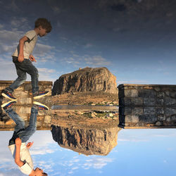 Side view of man on rock against sky