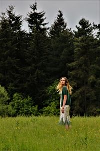 Young woman on grassy field against trees