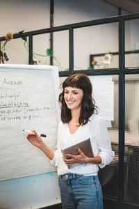 Smiling businesswoman holding digital tablet while writing business strategy in office