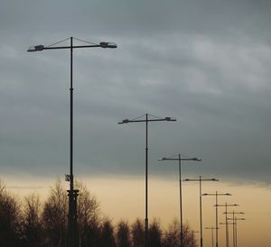 Low angle view of street lights against cloudy sky