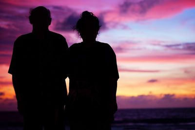 Rear view of silhouette couple standing at beach during sunset