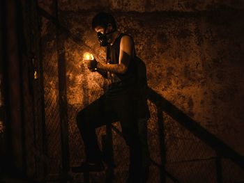 Low angle view of young man holding illuminated lighting equipment while moving up on steps in darkroom