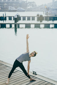 Full length of young man exercising by lake on boardwalk