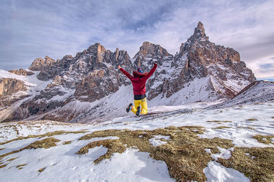 Jumping woman in snow covered mountains against sky
