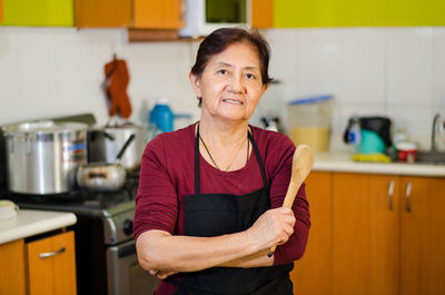 Portrait of woman holding wooden spoon while standing at home