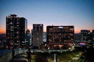 Illuminated buildings in city against clear sky at dusk