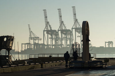 Silhouette man fishing at harbor against clear sky