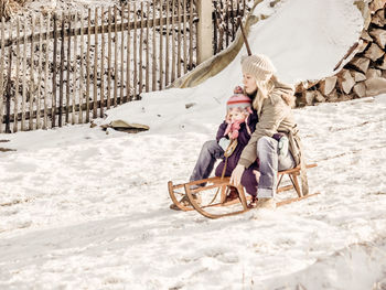 Mother and daughter sledding on snow covered field 