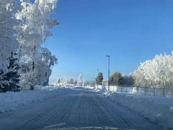 Snow covered road by trees against blue sky