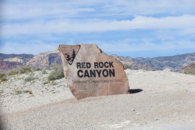 Information sign on rock by land against sky