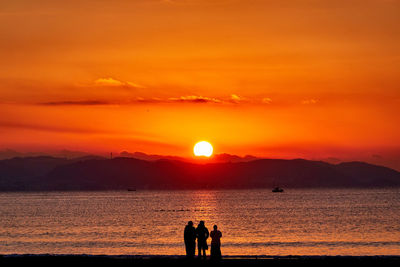 Silhouette people on beach against orange sky