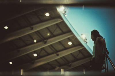 Low angle view of woman standing against illuminated ceiling