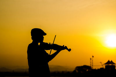 Silhouette boy playing violin against sky during sunset