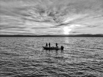 Silhouette people on boat in sea against sky