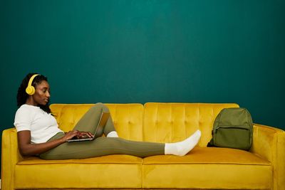 Afroamerican student laying at a yellow sofa front a dark green wall