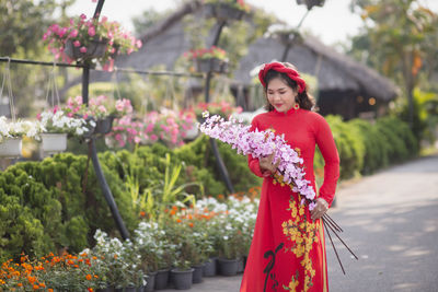 Portrait of smiling young woman standing by flowering plants