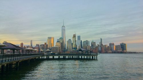 View of city at waterfront against cloudy sky