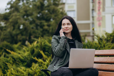 Young woman using laptop while sitting on bench