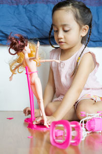 Cute girl playing with doll while sitting on floor at home