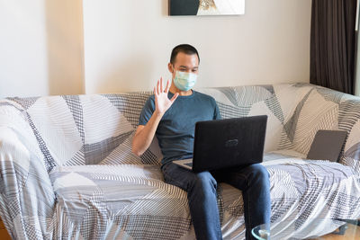 Full length of man using mobile phone while sitting on sofa