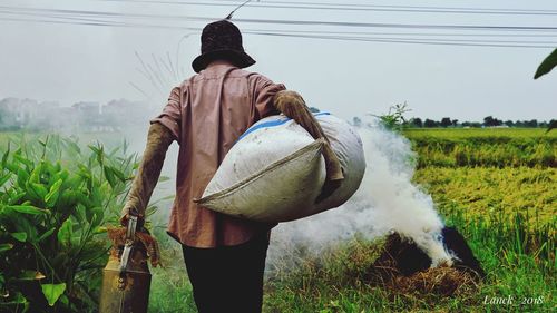 Rear view of farmer with sack walking by bonfire at farm