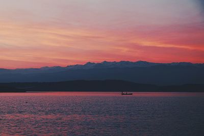 Scenic view of sea by mountains against orange sky during sunset